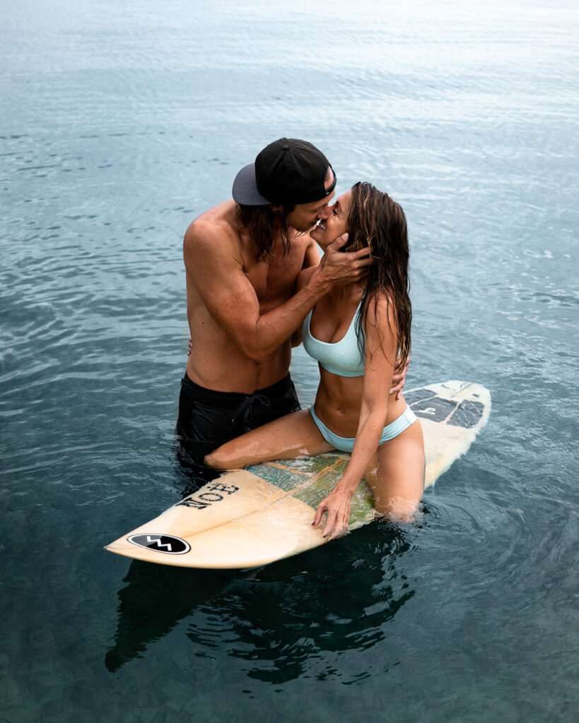 A man and woman kissing on a surfboard in the water.