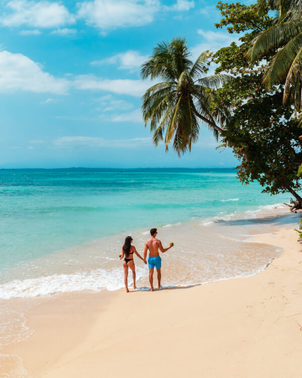 A man and woman holding hands on the beach.